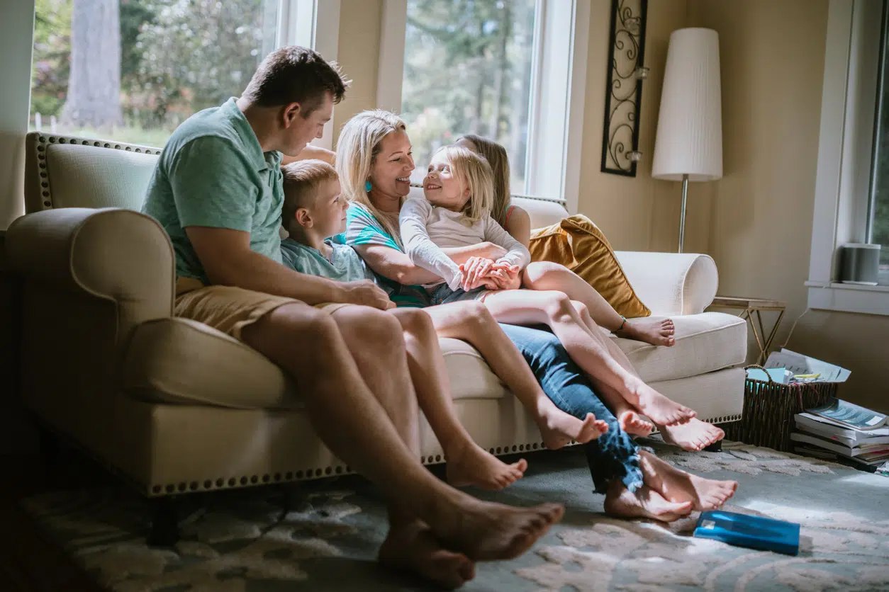 Happy Family Cuddling on Living Room Couch at Home A young family snuggles up on the couch in their living room, smiling and enjoying being close and together. Part of a regular routine, or the new normal during the Covid-19 pandemic and the stay at home order. Shot in Washington State, USA.